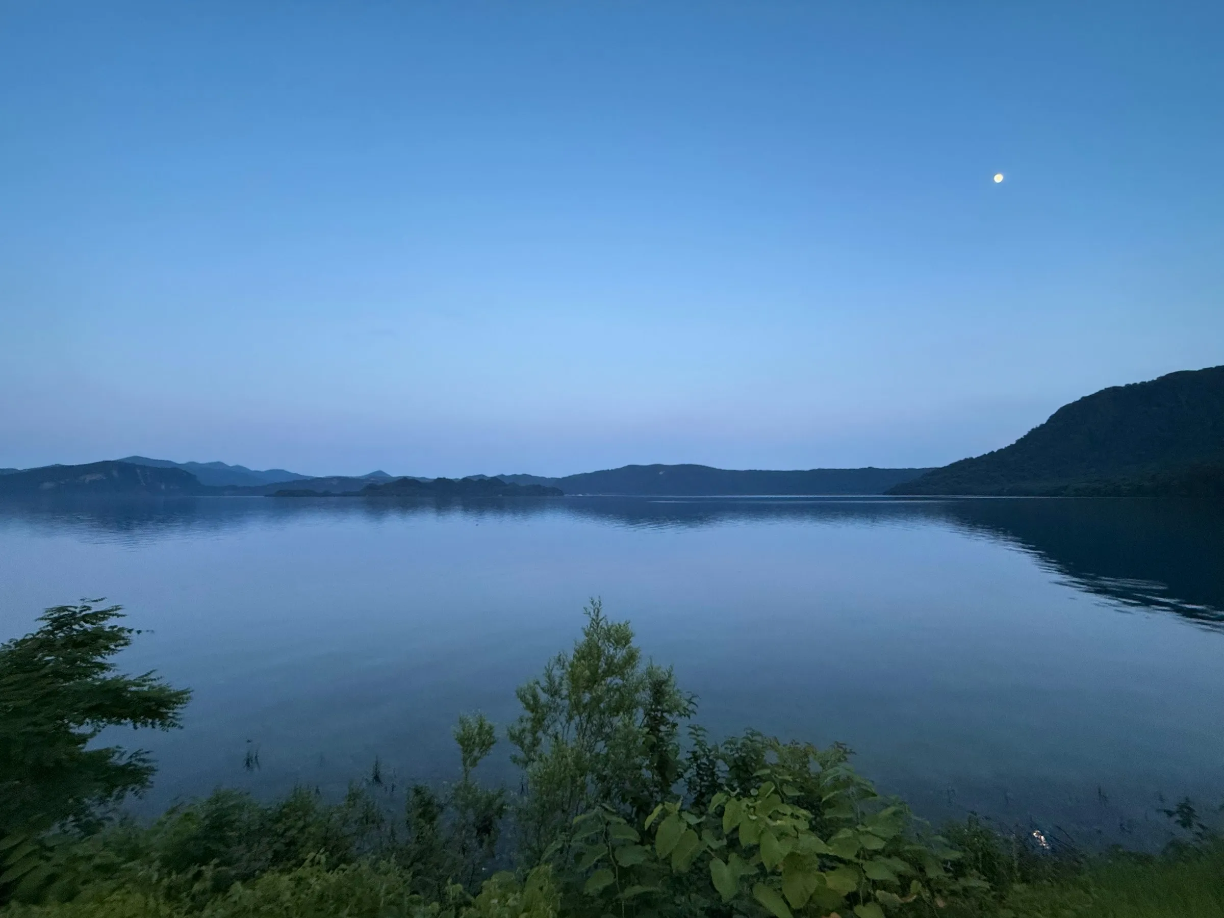 夕暮れの十和田湖。対岸の山並みと、空に浮かぶ月。
